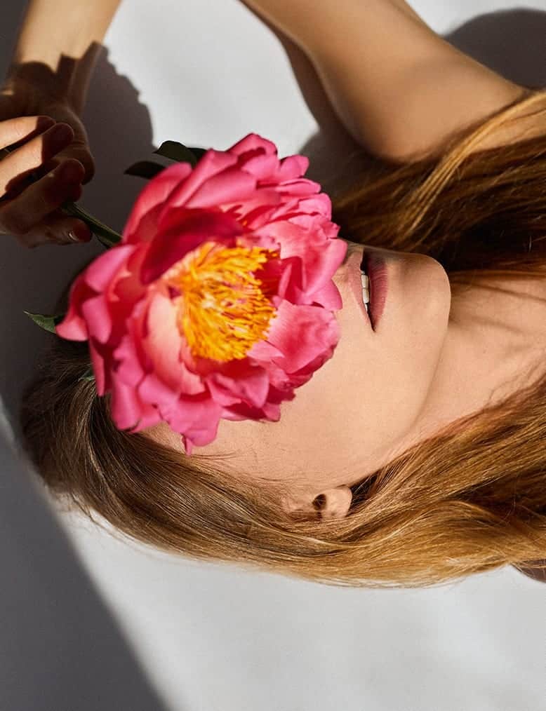 Leżąca osoba zasłania twarz kwiatem trzymanym w dłoni.