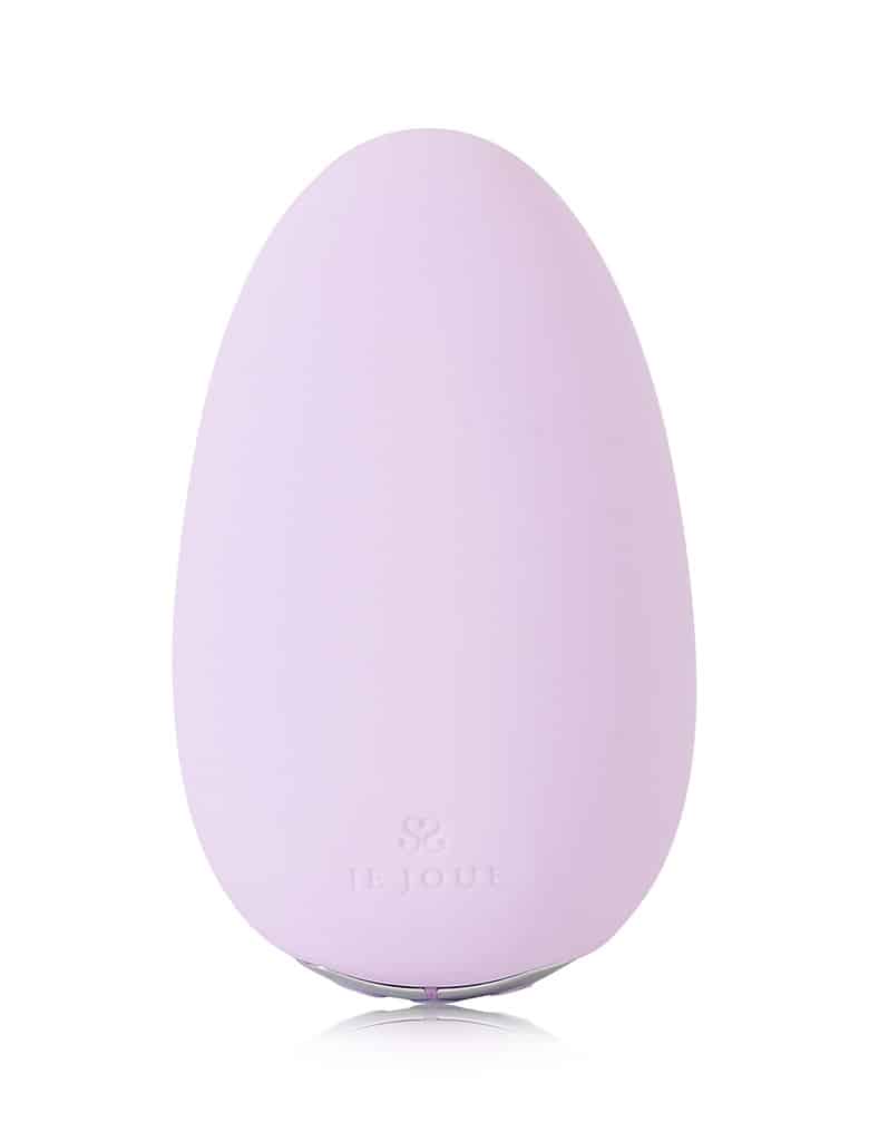 Masażer Mimi Soft w kolorze lilowym ma kształt spłaszczonego jajka z wytłoczonym na powierzchni niedużym logo Je Joue.
