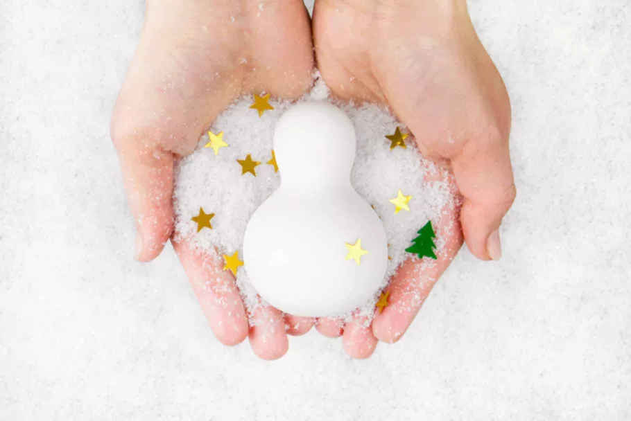 Masażer-bałwanek Iroha Yuki leży w dłoniach posypanych śniegiem i złotym konfetti w kształcie gwiazdek.