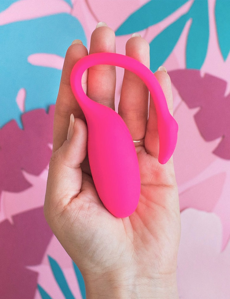Wibrująca kulka Magic Motion Flamingo leży na otwartej dłoni. W tle widać wycięte z papieru kolorowe, egzotyczne liście.
