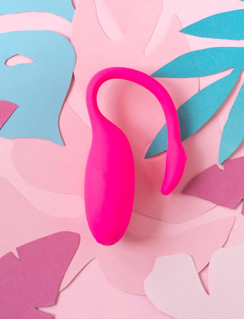 Wibrująca kulka Magic Motion Flamingo leży na tle papierowych, egzotycznych liściach w kolorach różu i zieleni.