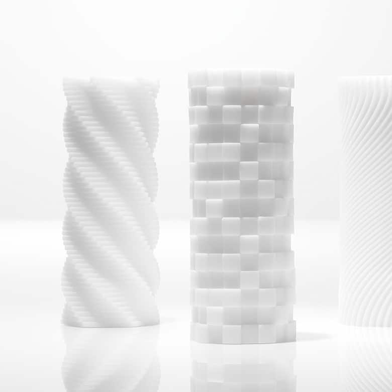 Obok siebie stoją trzy białe masturbatory Tenga 3D z elastomeru. Mają kształt okrągłych wież z wyżłobionymi wzorami.