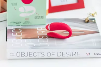 Na książce o tytule "Objects of desire" leży czerwony wibrator dla par Moqqa Reef by We-Vibe i jego opakowanie.