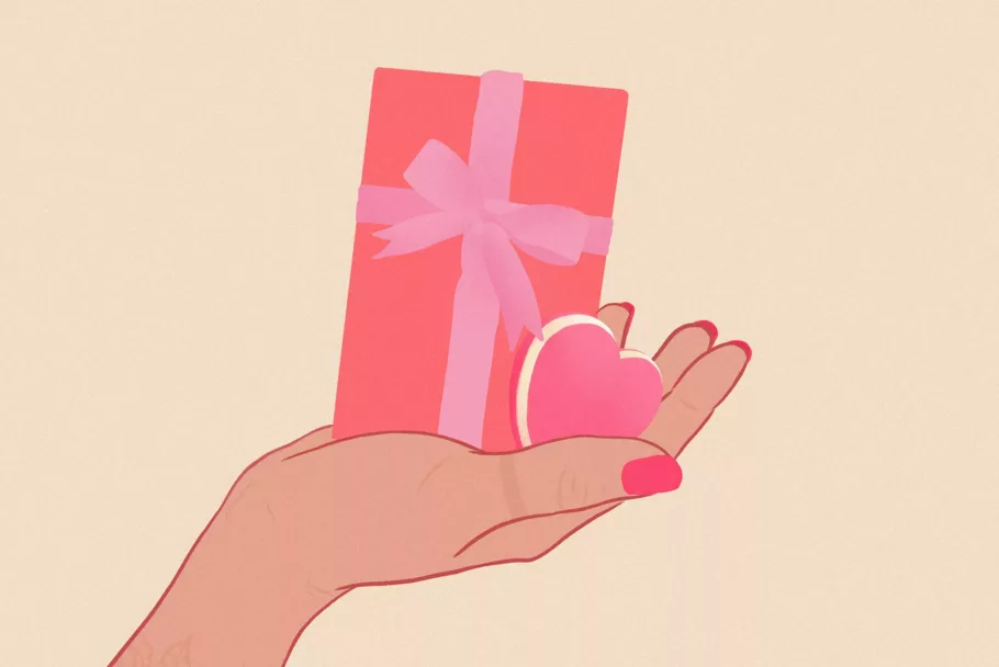 Na rysunku na otwartej dłoni leży czerwone prezentowe pudełko z różową kokardą i różowy masażer łechtaczki w kształcie serca.