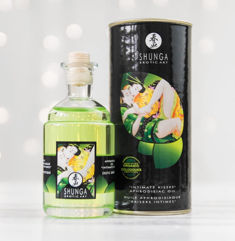 Buteleczka z korkiem i zielonym olejkiem oraz zewnętrzna tuba Shunga Aphrodisiac Oil są ozdobione rysunkiem przytulonej pary.