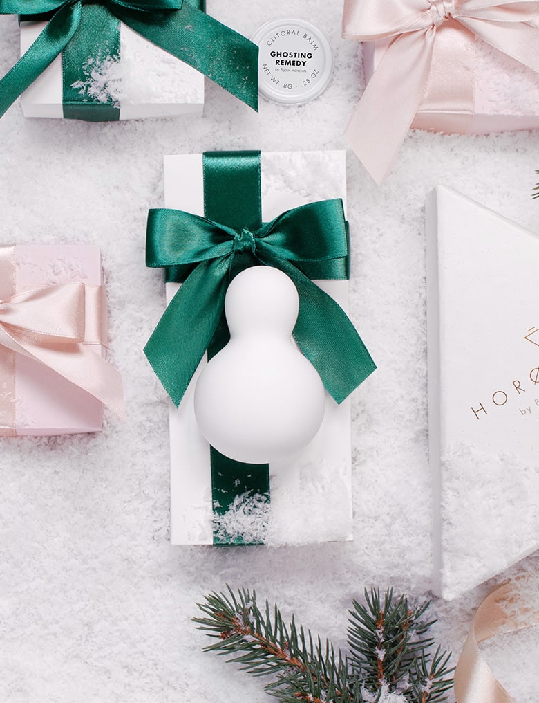 Iroha Yuki, biały masażer łechtaczki w kształcie bałwanka leży na zaśnieżonej powierzchni wśród prezentowych pudełek.