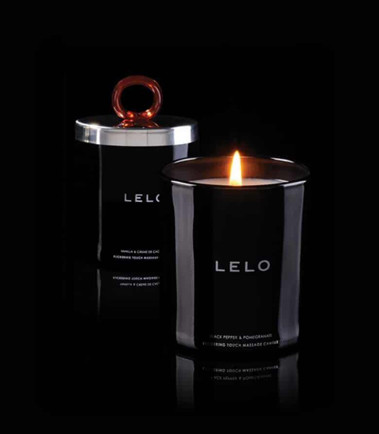 Na pierwszym planie pali się świeca do masażu LELO. Na czarnym tle widać drugą świecę przykrytą wieczkiem.