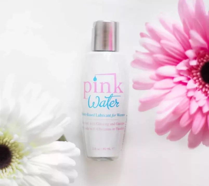 Buteleczka lubrykantu Pink Water leży między różowym i białym kwiatem.