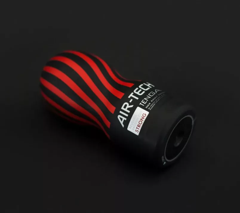Na czarnym tle leży masturbator Tenga Air-Tech Strong z czarno-czerwoną etykietą i podstawą z okrągłym wgłębieniem na środku.