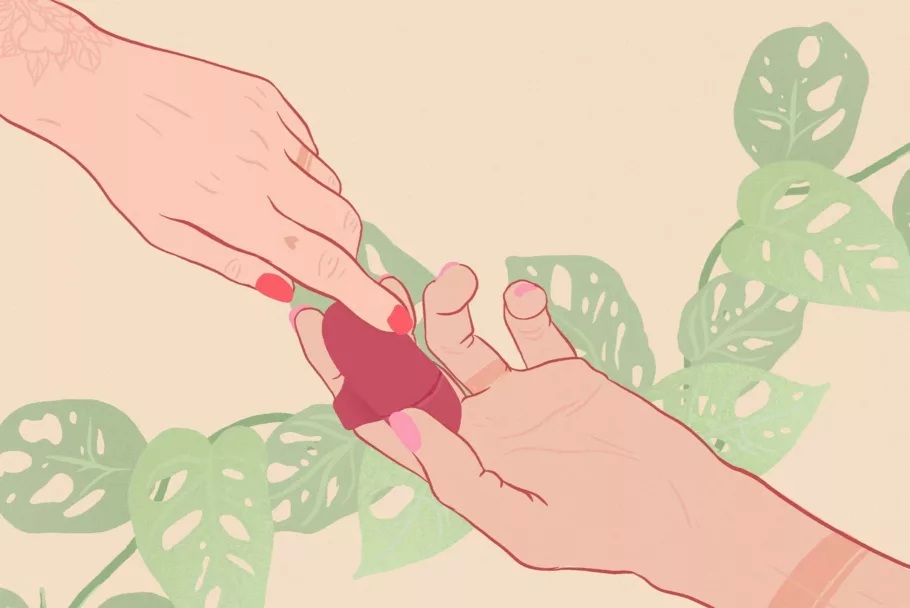 Na rysunku masażer łechtaczki jest założony na palec jednej dłoni. Druga dłoń dotyka powierzchni gadżetu. W tle widać liście.