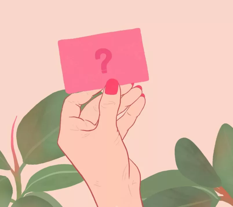 Dłoń z czerwonymi paznokciami trzyma kartę z narysowanym znakiem zapytania. W tle widać liście rośliny doniczkowej.